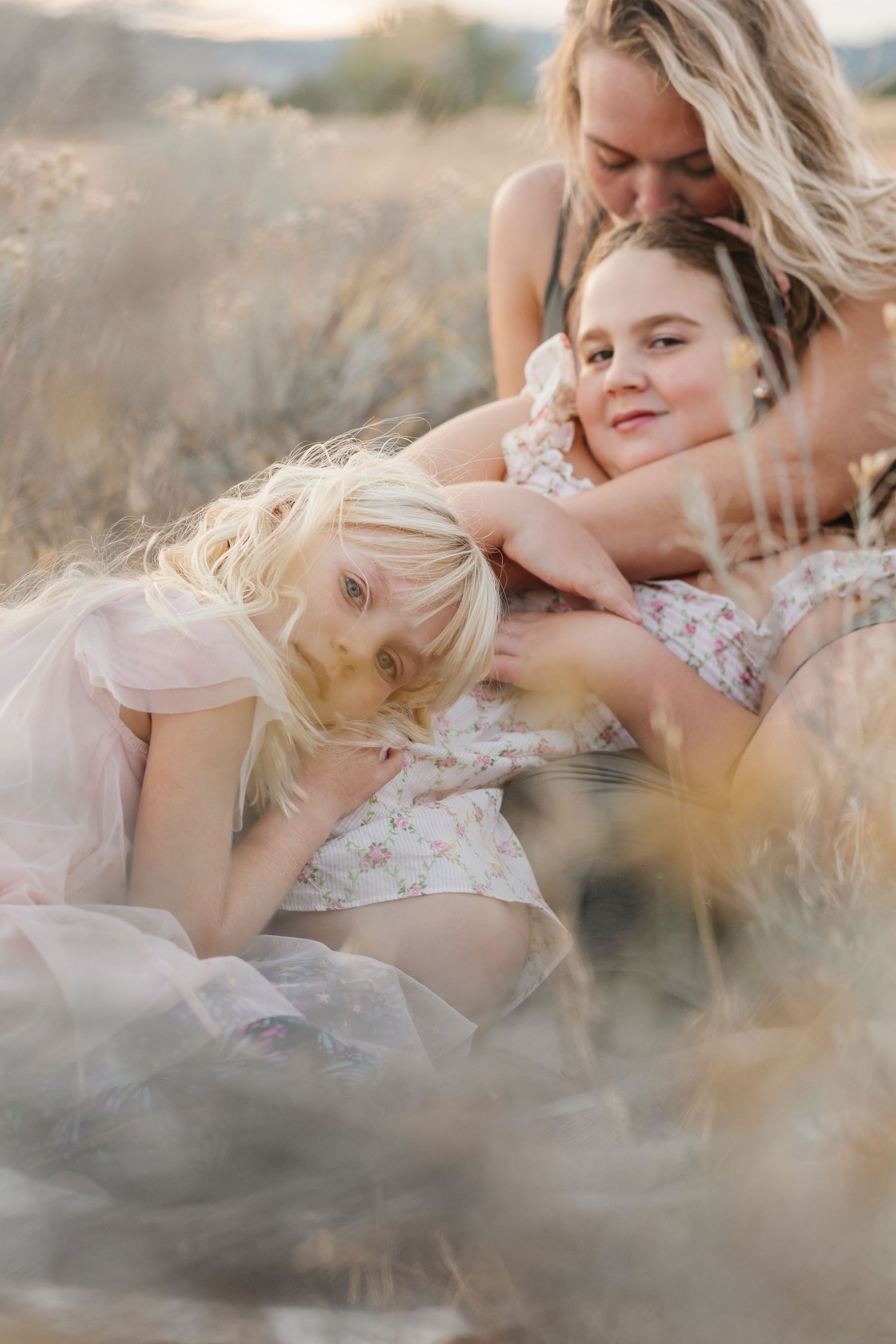A tender moment captured in golden light as a mother and daughter lie in a field of tall grass at sunset.