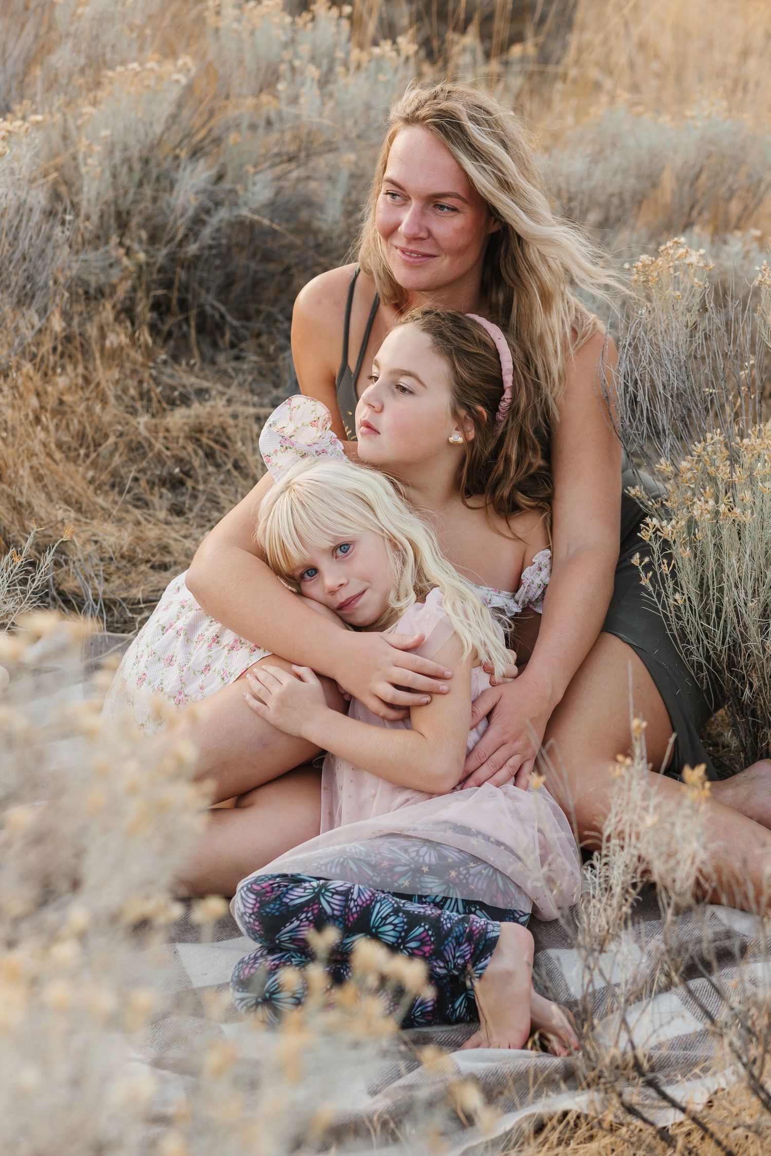 A tender family moment captured outdoors among dried grass and brush during golden hour.