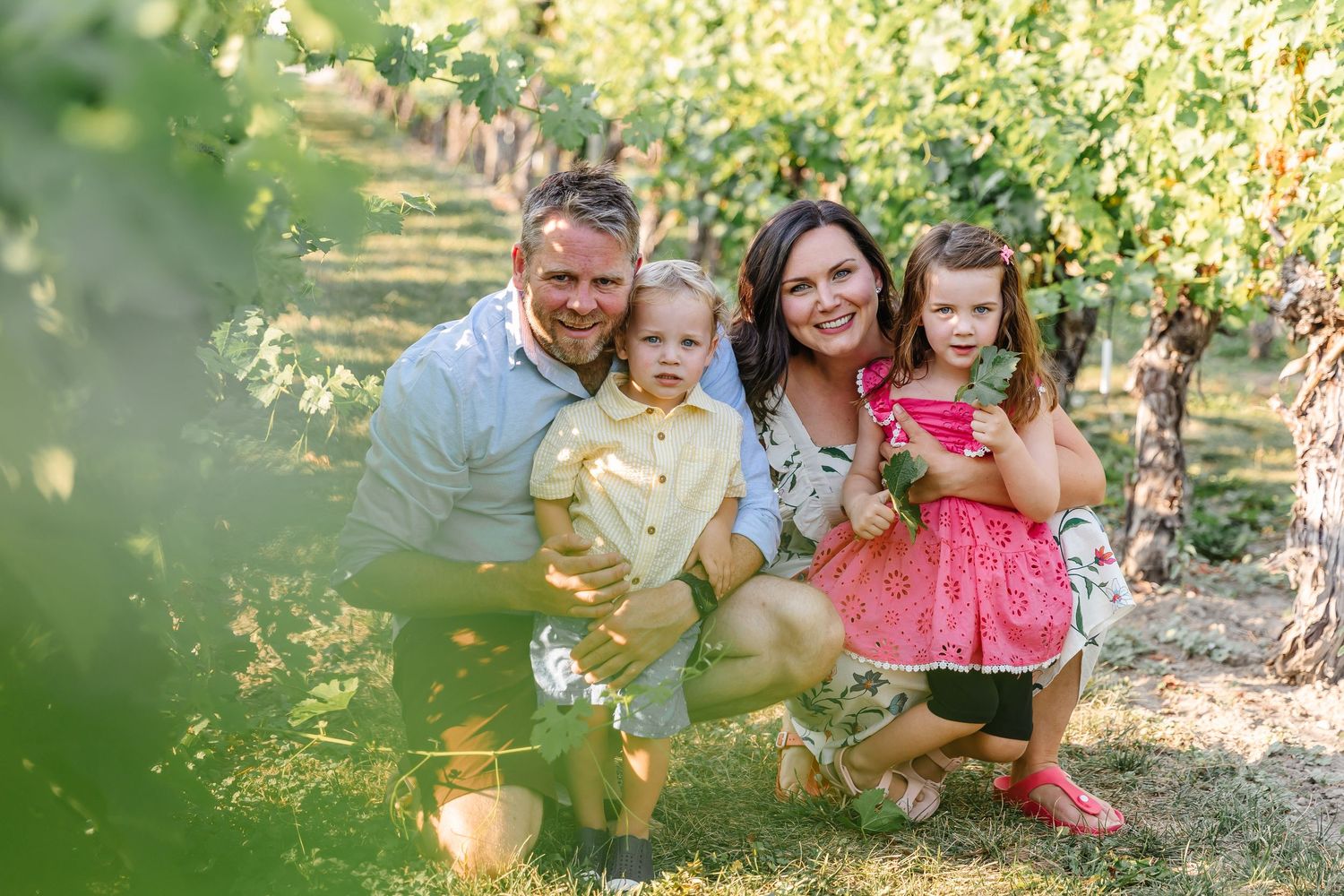 Family photoshoot in a lush garden setting with sunlight filtering through the leaves at quails gate in west Kelowna