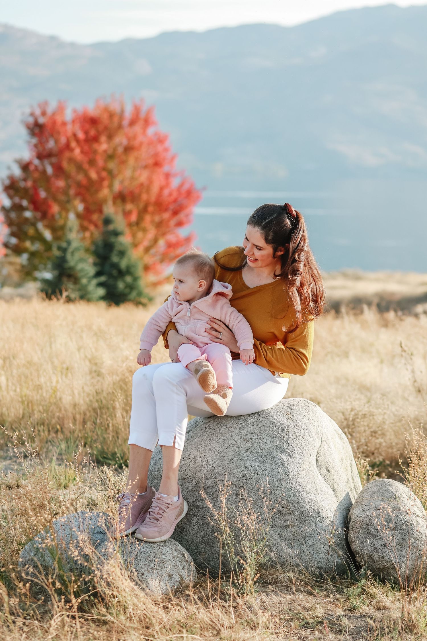An intimate outdoor portrait sitting on a boulder with mountains and fall colors in the background in West Kelowna at sanctuary gardens