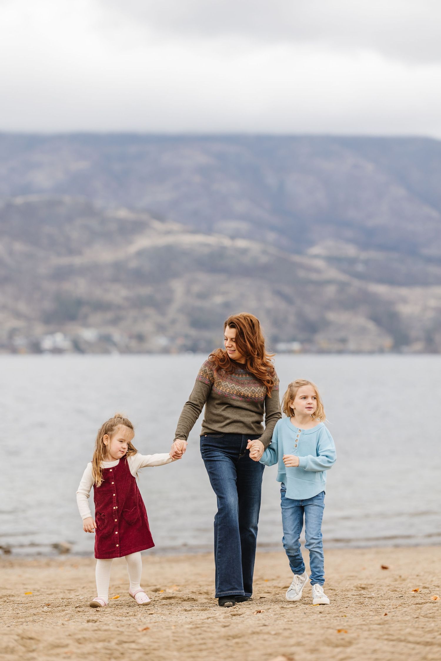 Family walking together along a scenic beach with mountains in the background on an overcast day.