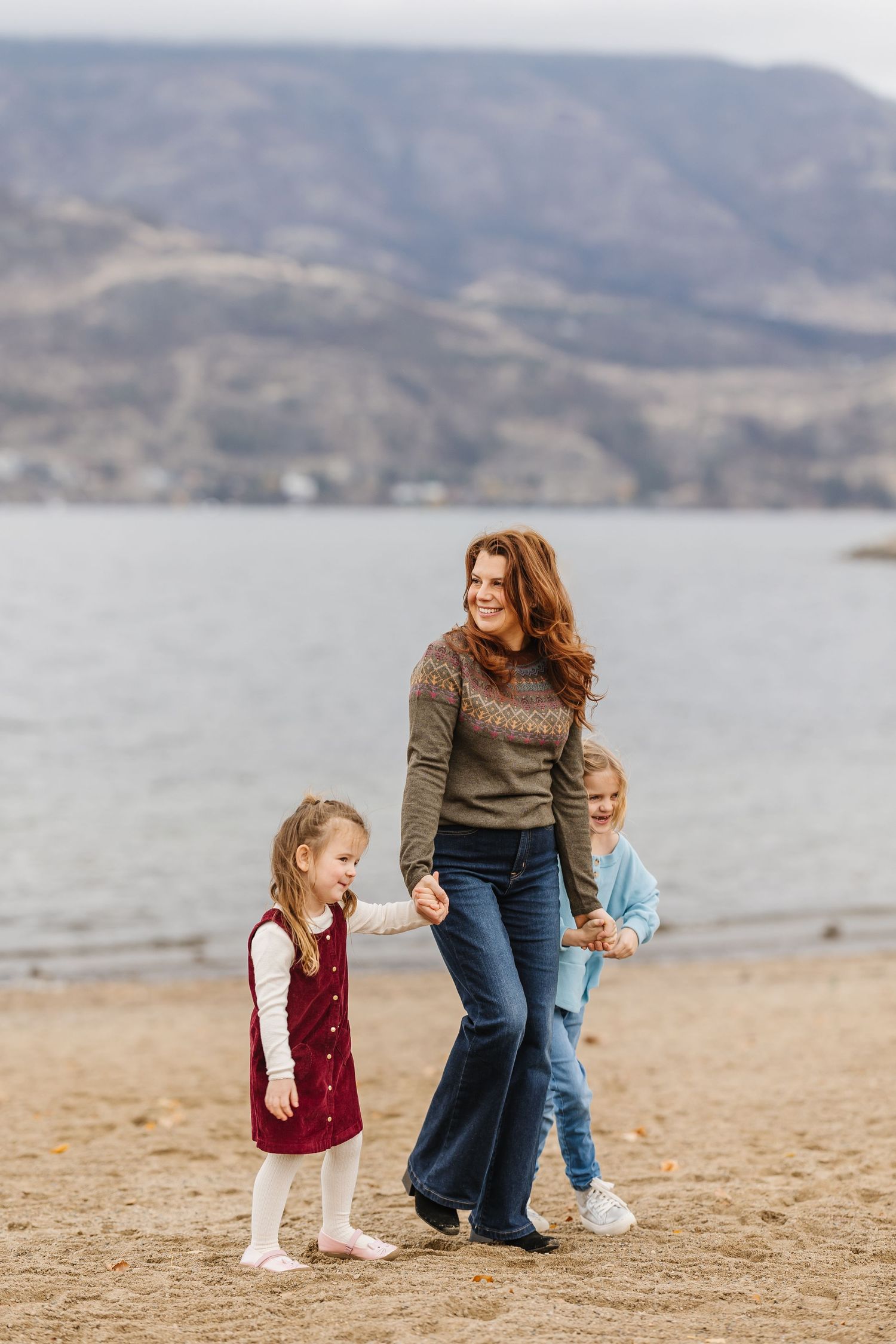 Family playing together on a sandy beach with mountains and water in the background on an overcast day.