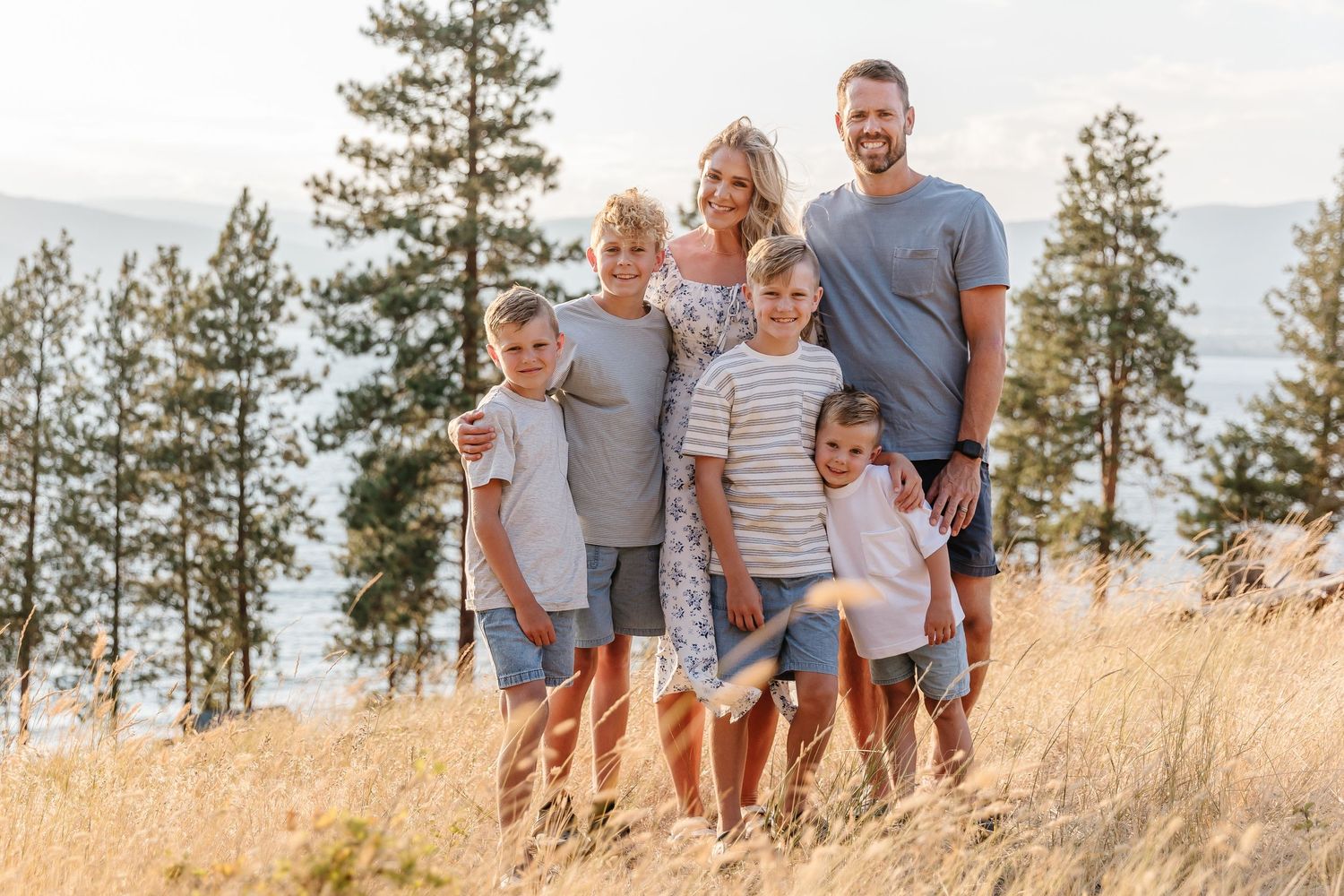 A family stands together in casual attire against a backdrop golden grass at sunset for a family photoshoot in kelowna at Bertram creek park