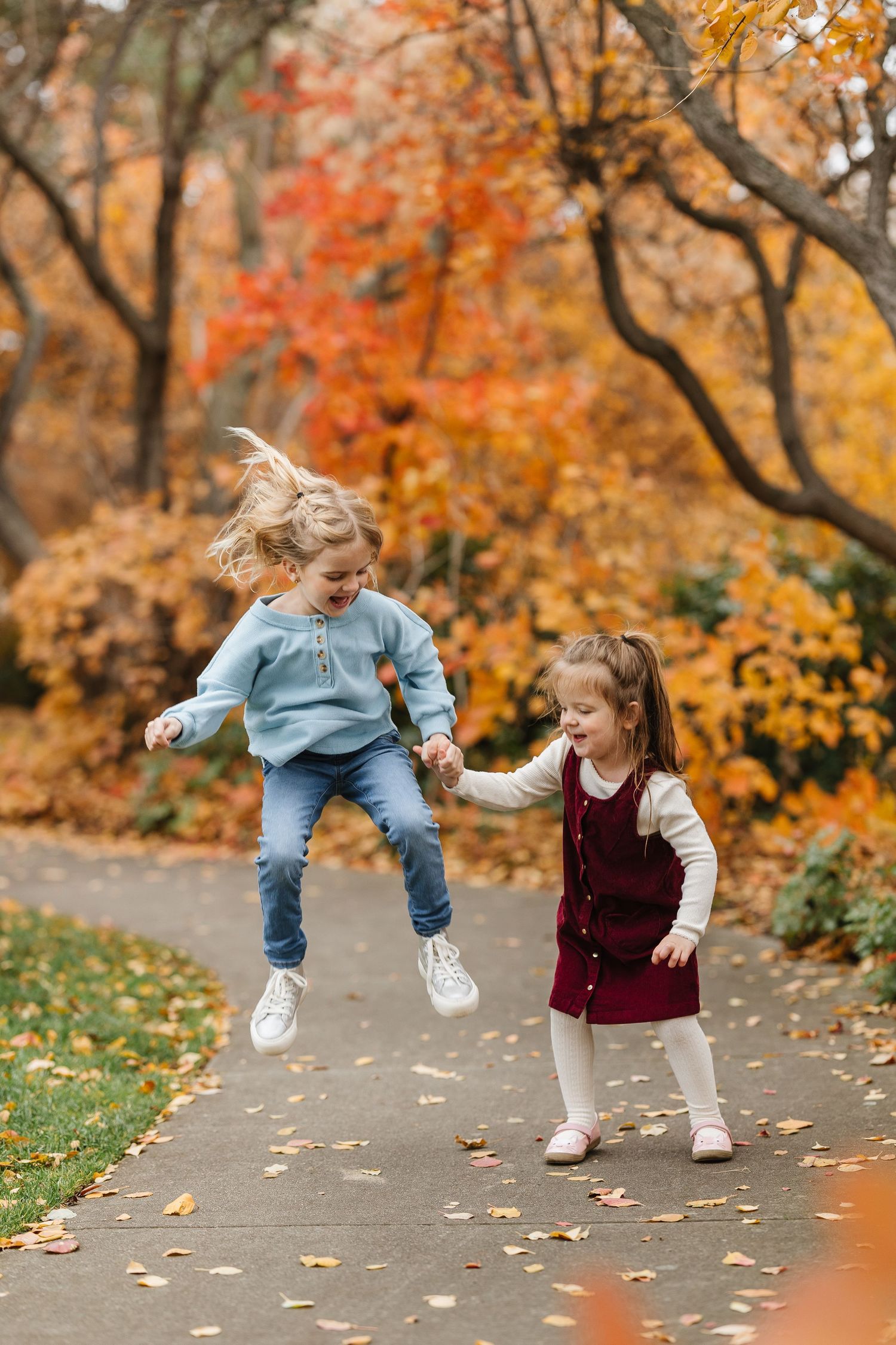 Children playing and jumping together on a path surrounded by vibrant autumn foliage.