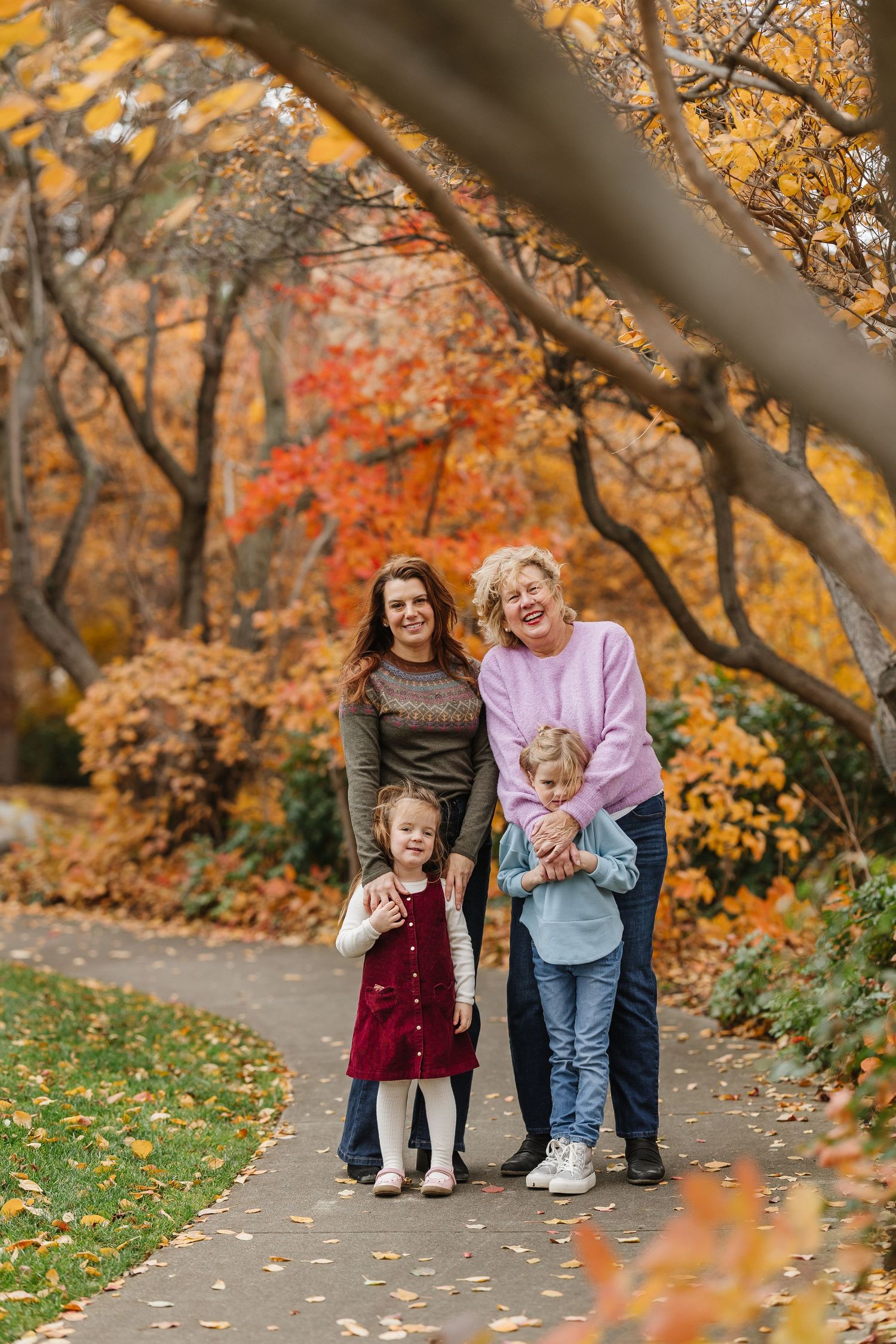 A group poses together under vibrant autumn trees with golden and orange leaves on a path covered in fallen foliage.