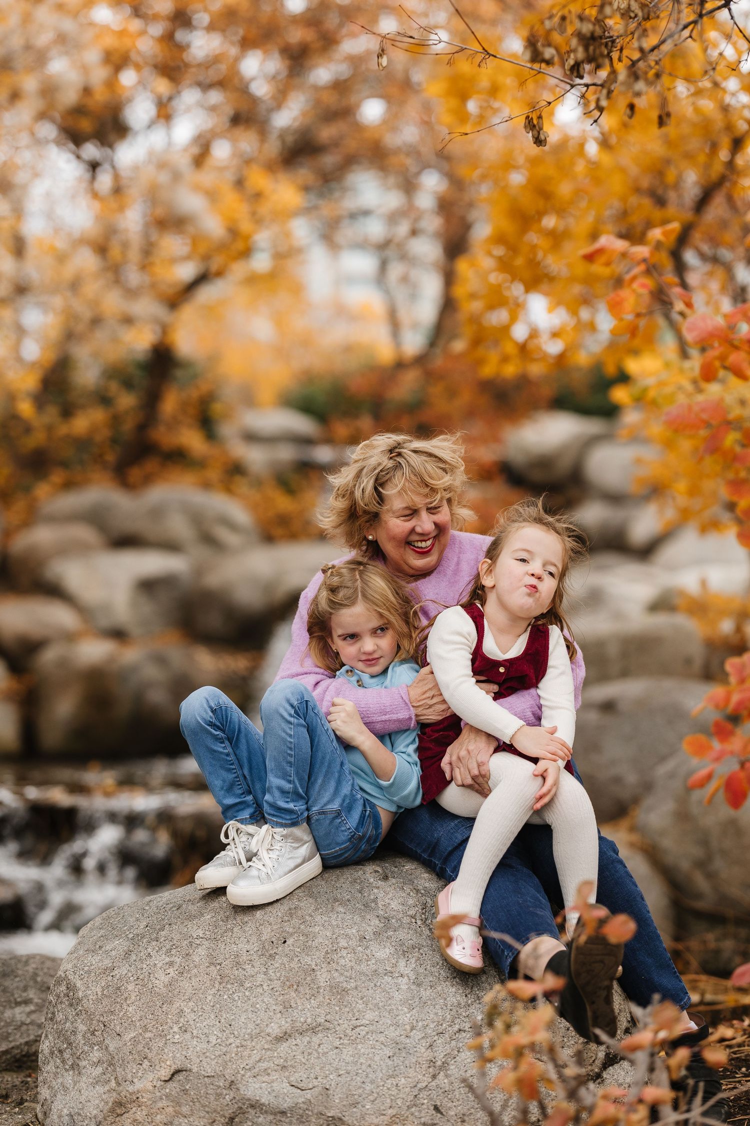 Three candid photos show people sitting on a large rock surrounded by vibrant autumn foliage in a natural outdoor setting.