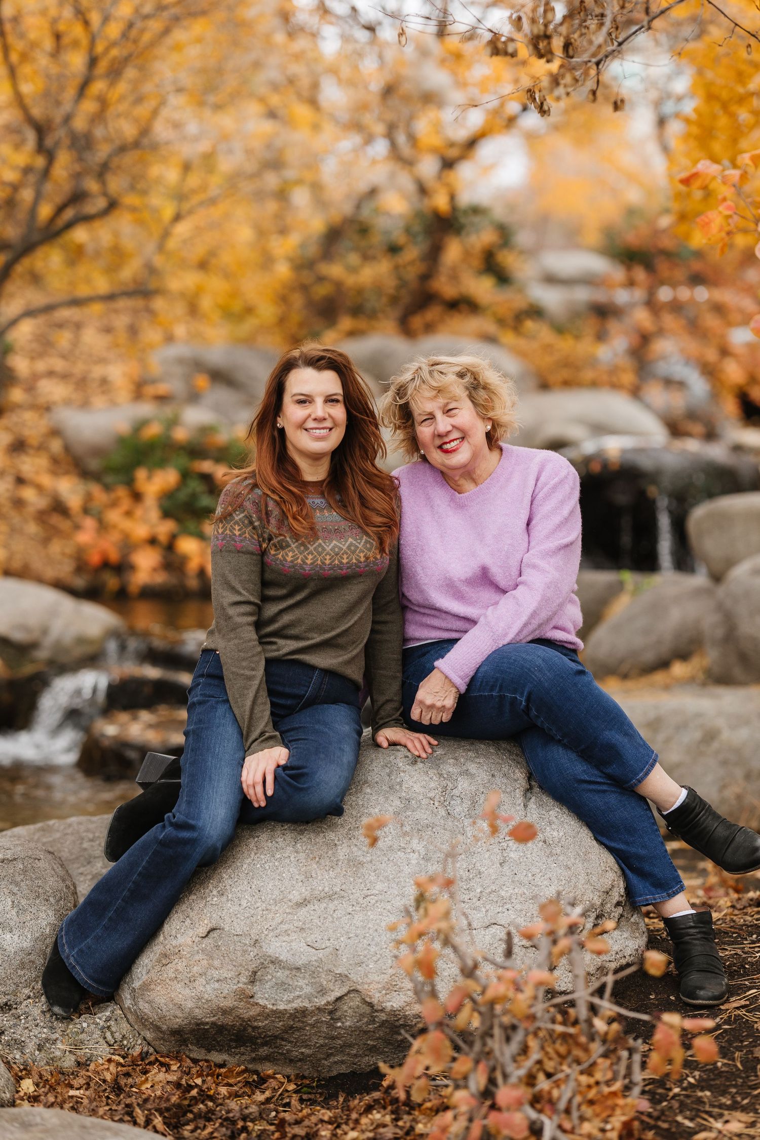 Two people sitting and laughing together on large rocks surrounded by fall colors and foliage.