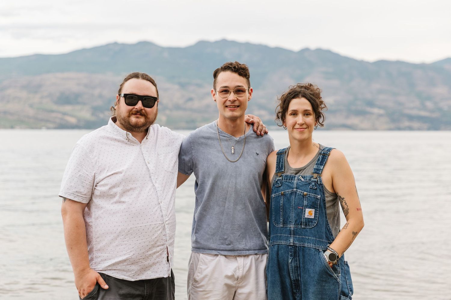 A group of people in casual attire pose together on a beach with mountains visible in the background.