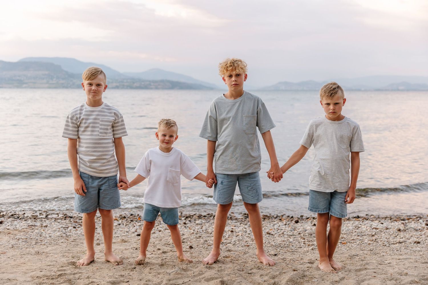 Row of kids standing together on a rocky beach with mountains visible in the distance in kelowna at Bertram park creek for family photo's