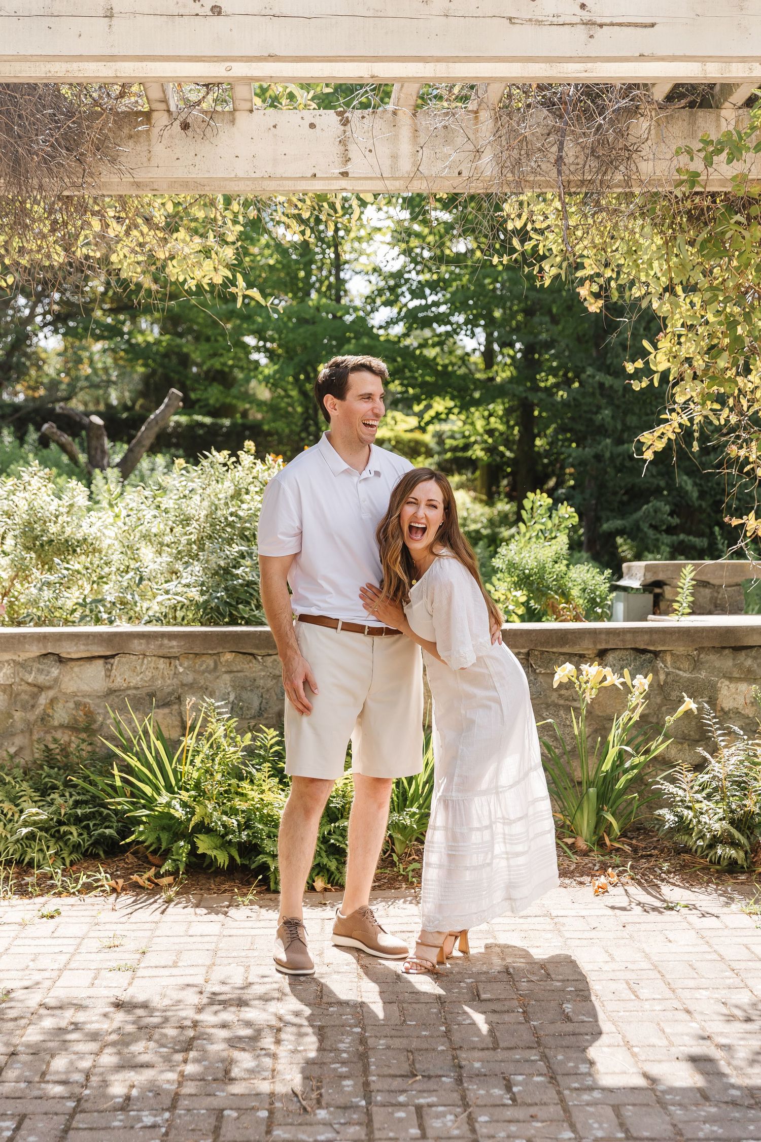 A couple shares a joyful moment together in a sunlit garden setting with stone architecture and lush greenery.