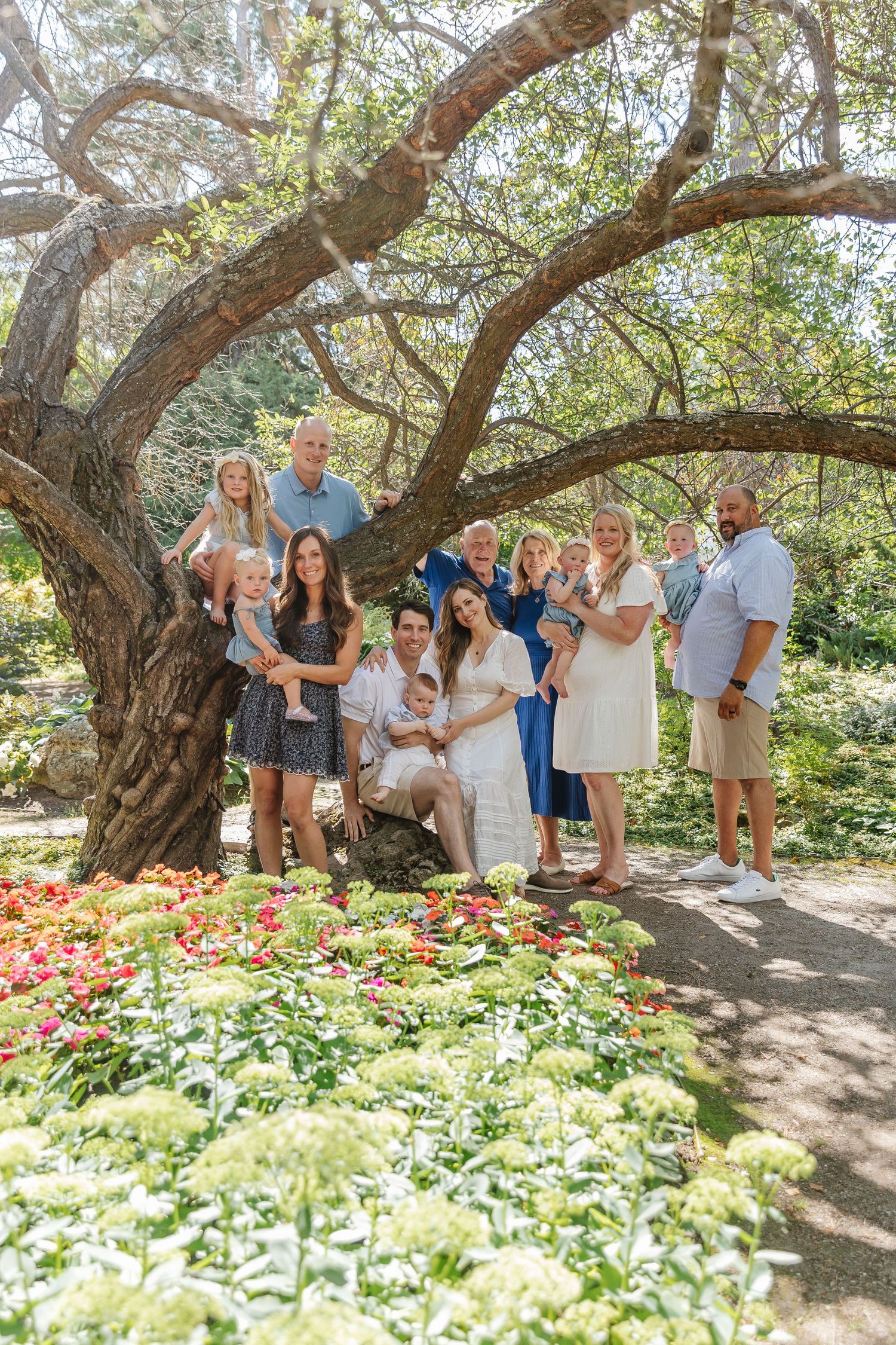 A group poses together under a large branching tree with colorful flowers blooming in the garden below.