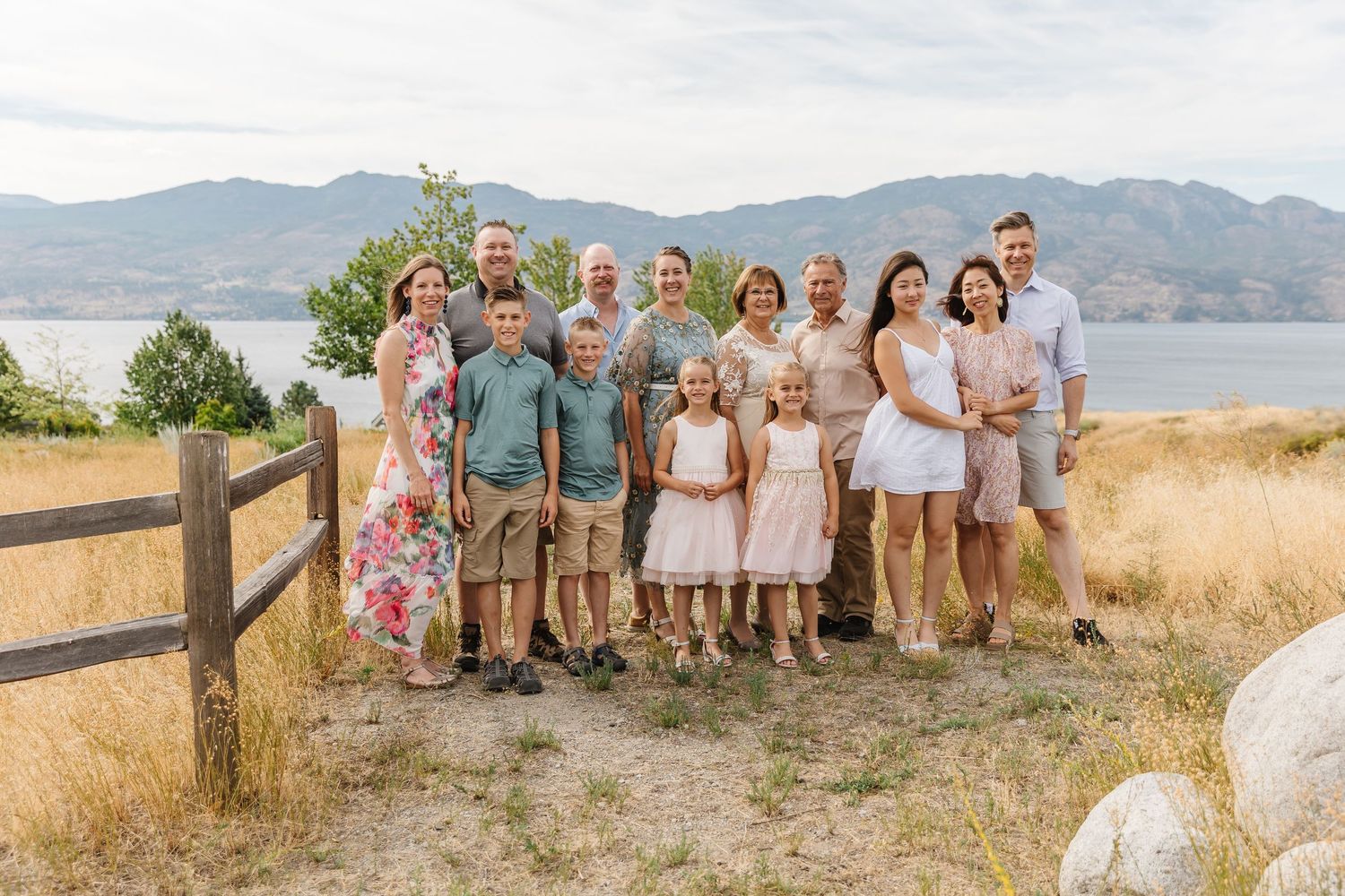 A group poses together on a hilltop with a wooden fence and mountain lake vista in the background.