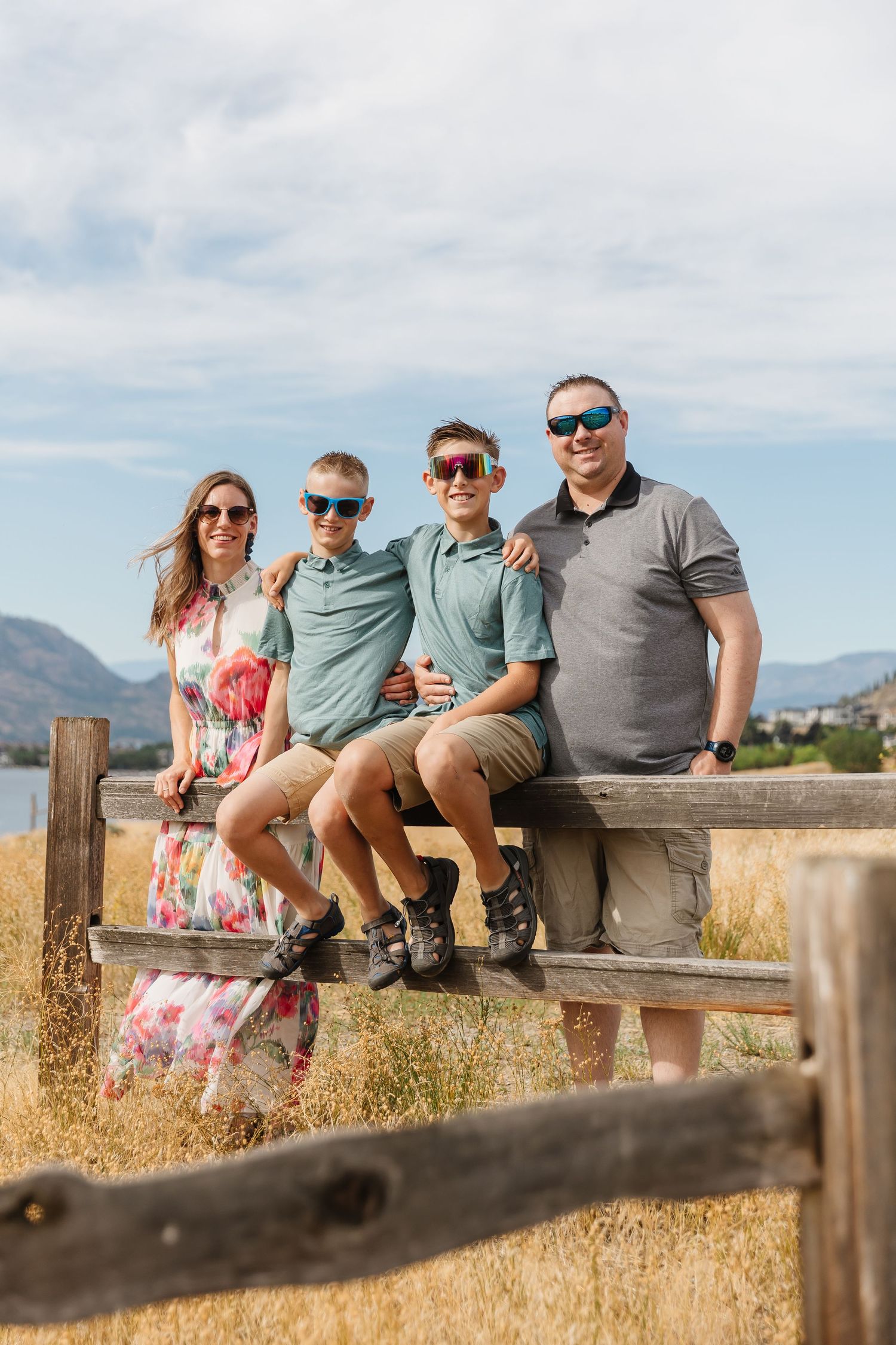 A group sits on a wooden fence overlooking mountains and dry grassland on a sunny summer day.