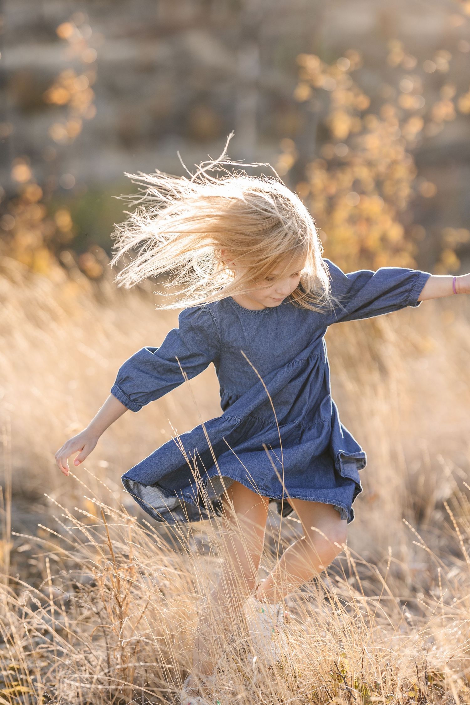 A person in a blue dress dances gracefully through golden wheat fields at sunset, their hair flowing in the wind.