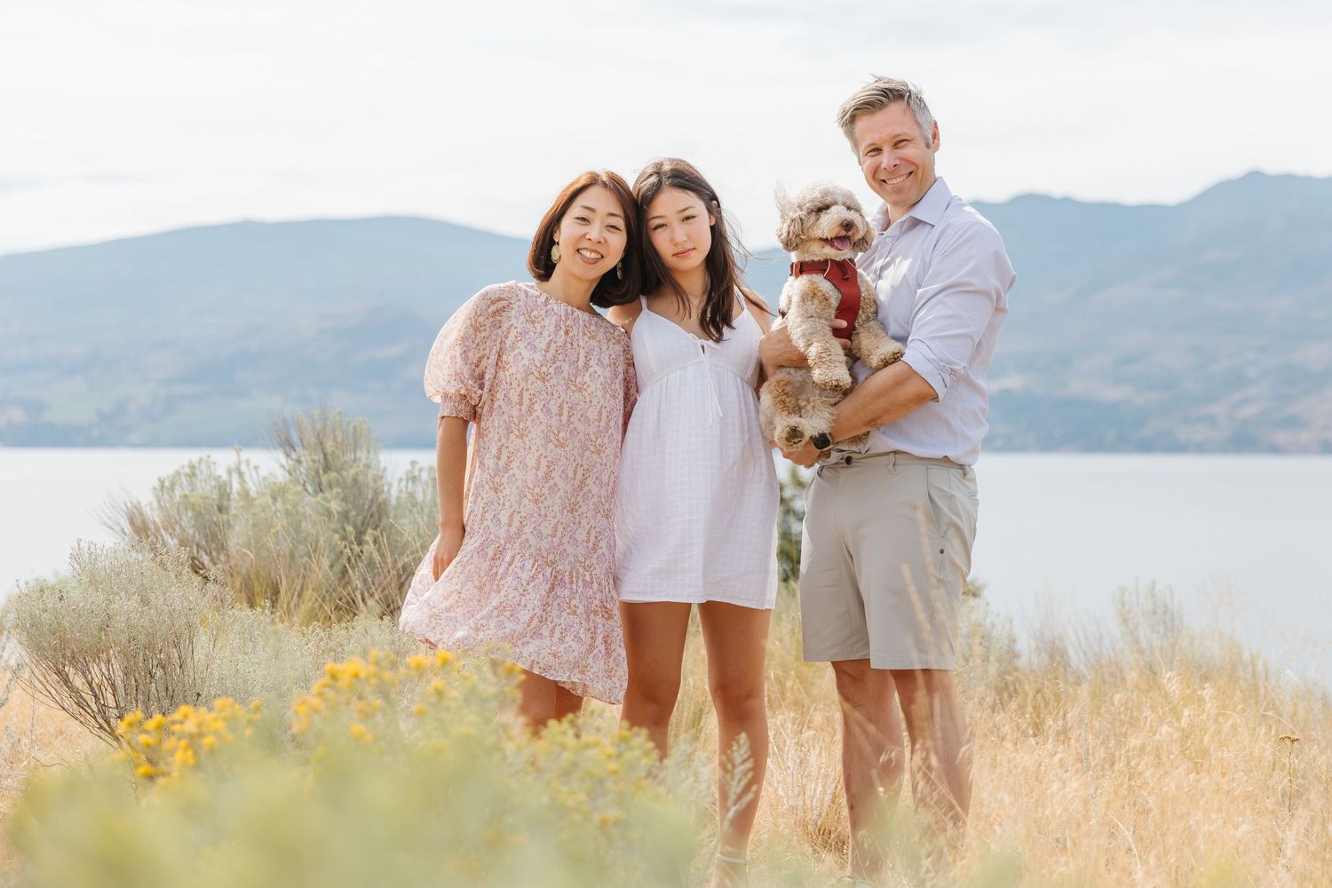 A group stands together on a hillside overlooking a serene lake with mountains in the background on a sunny day.