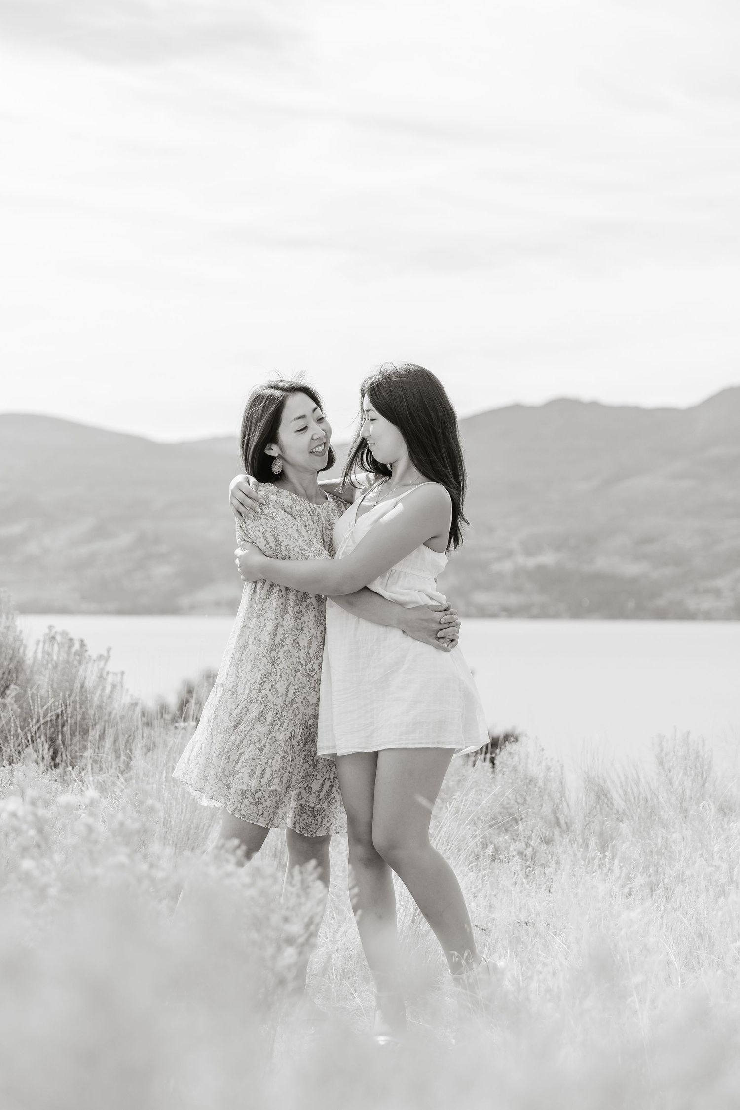 Two figures embrace joyfully in a sun-drenched meadow with mountains and a lake in the background.