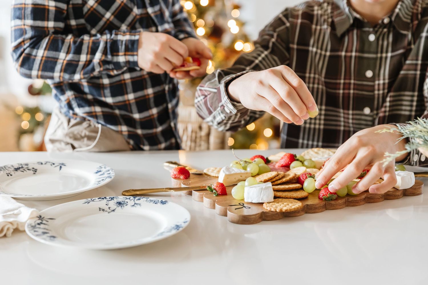 Hands in plaid shirt decorating Christmas cookies with white icing and colorful sprinkles on a festive table.