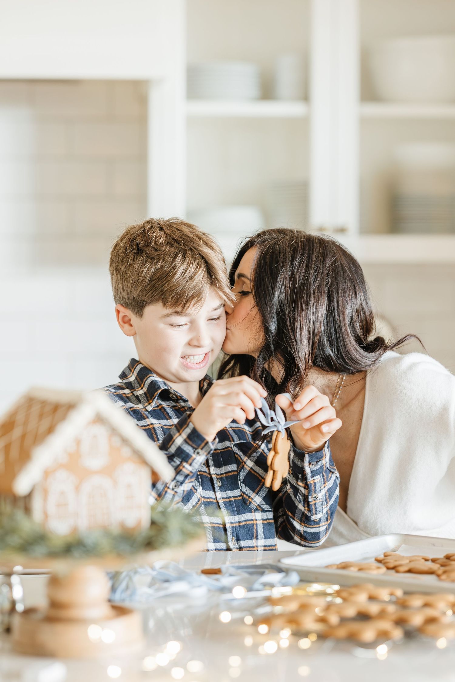 Intimate family moment captured in a bright kitchen with holiday decorations visible in background.