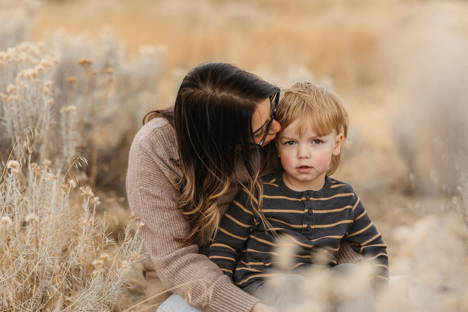 A family embraces in a golden field during sunset, wearing earth-toned clothing that complements the autumn landscape.