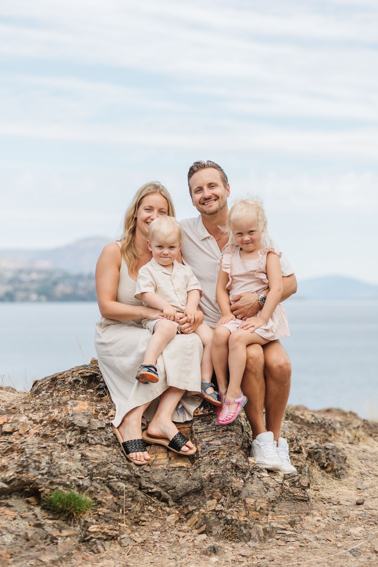 A happy family sitting together on a rocky outcrop with a serene lake view behind them.