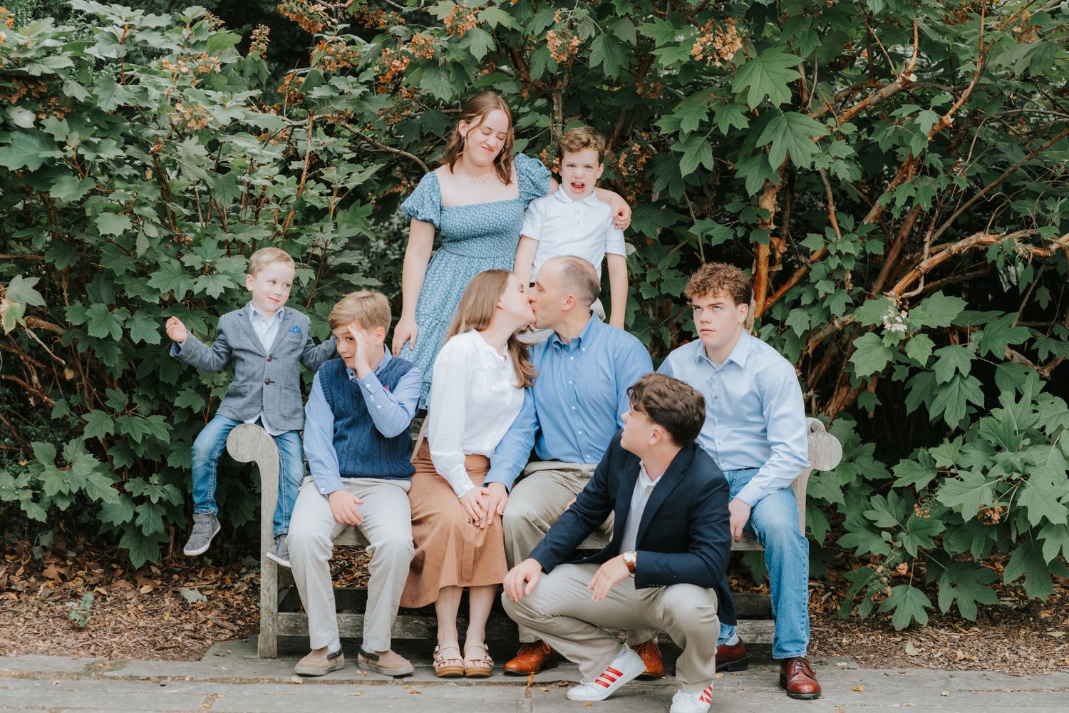 A group in coordinating blue and white outfits poses casually together against a lush green foliage backdrop.