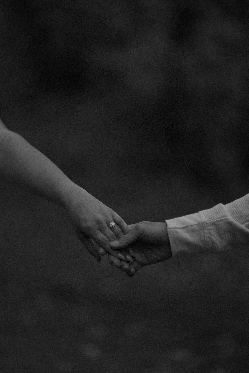 Black and white photo of a couple holding hands, with an engagement ring visible on the woman's finger.