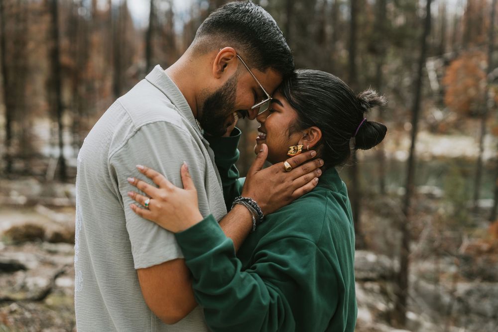 Couple embracing tenderly in a forest setting, sharing an intimate moment surrounded by trees.