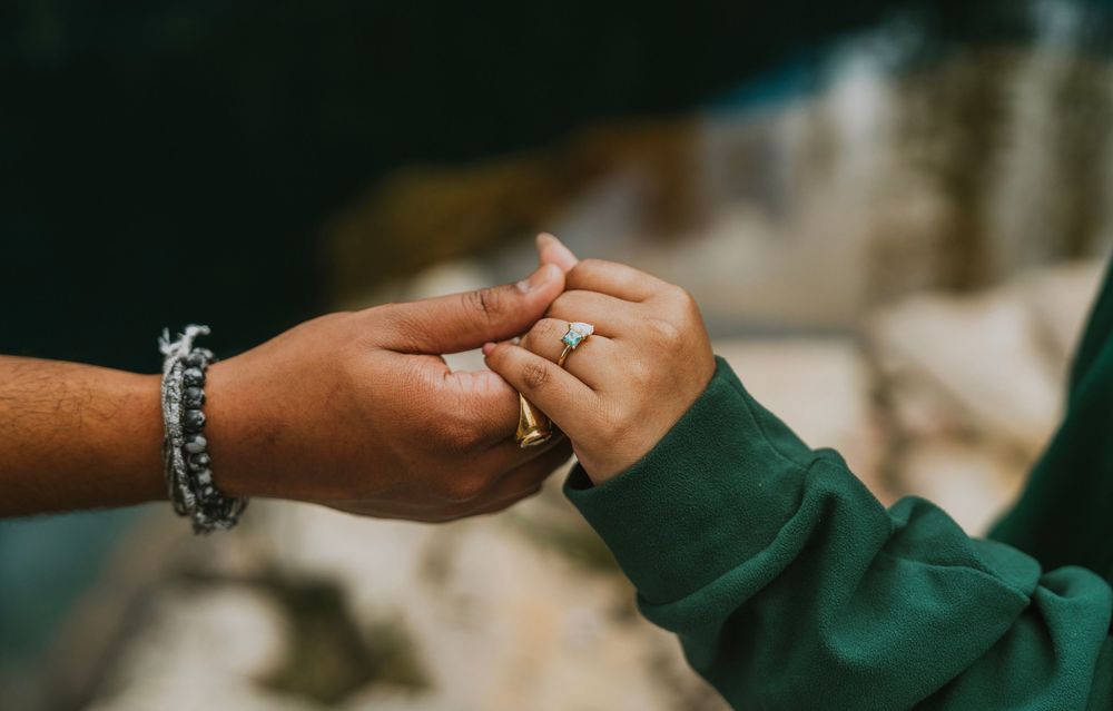 Close-up of a couple holding hands, showcasing a sparkling diamond engagement ring on the woman's finger.