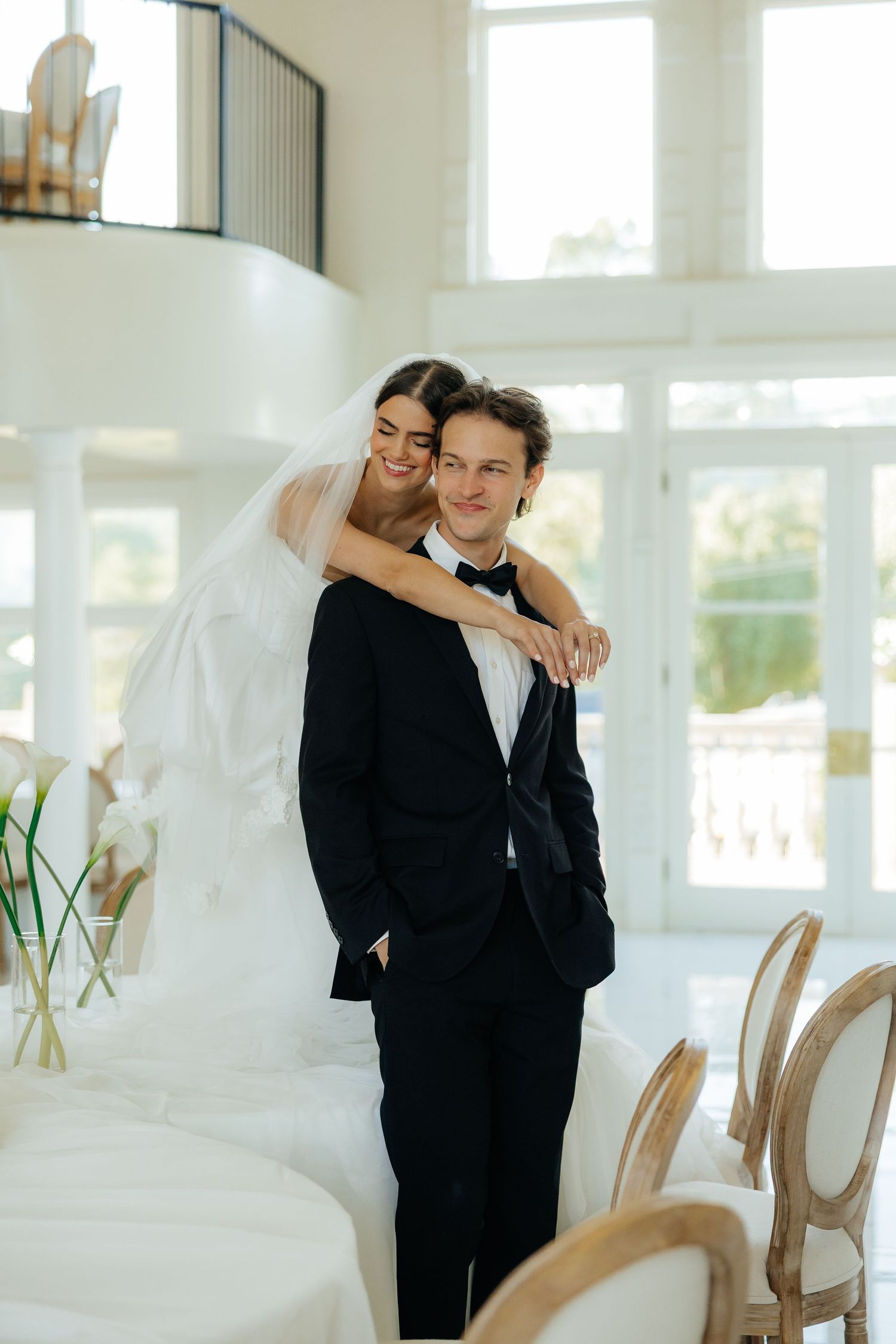 A romantic wedding scene with a couple embracing in front of white hydrangea flowers at sunset.