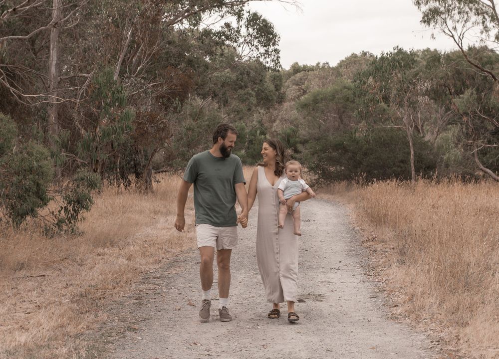 A couple walks together on a dirt path through dry grass and eucalyptus trees on a warm afternoon.