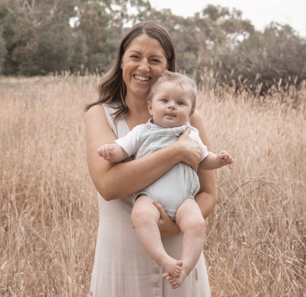 A mother and baby share joyful moments together in a sun-lit field of tall brown grass.