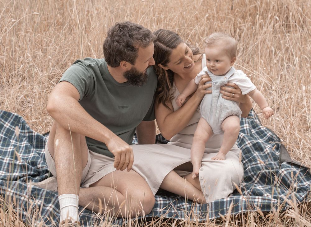 Family sitting together on picnic blanket in tall sepia-toned grass field during outdoor photo session.