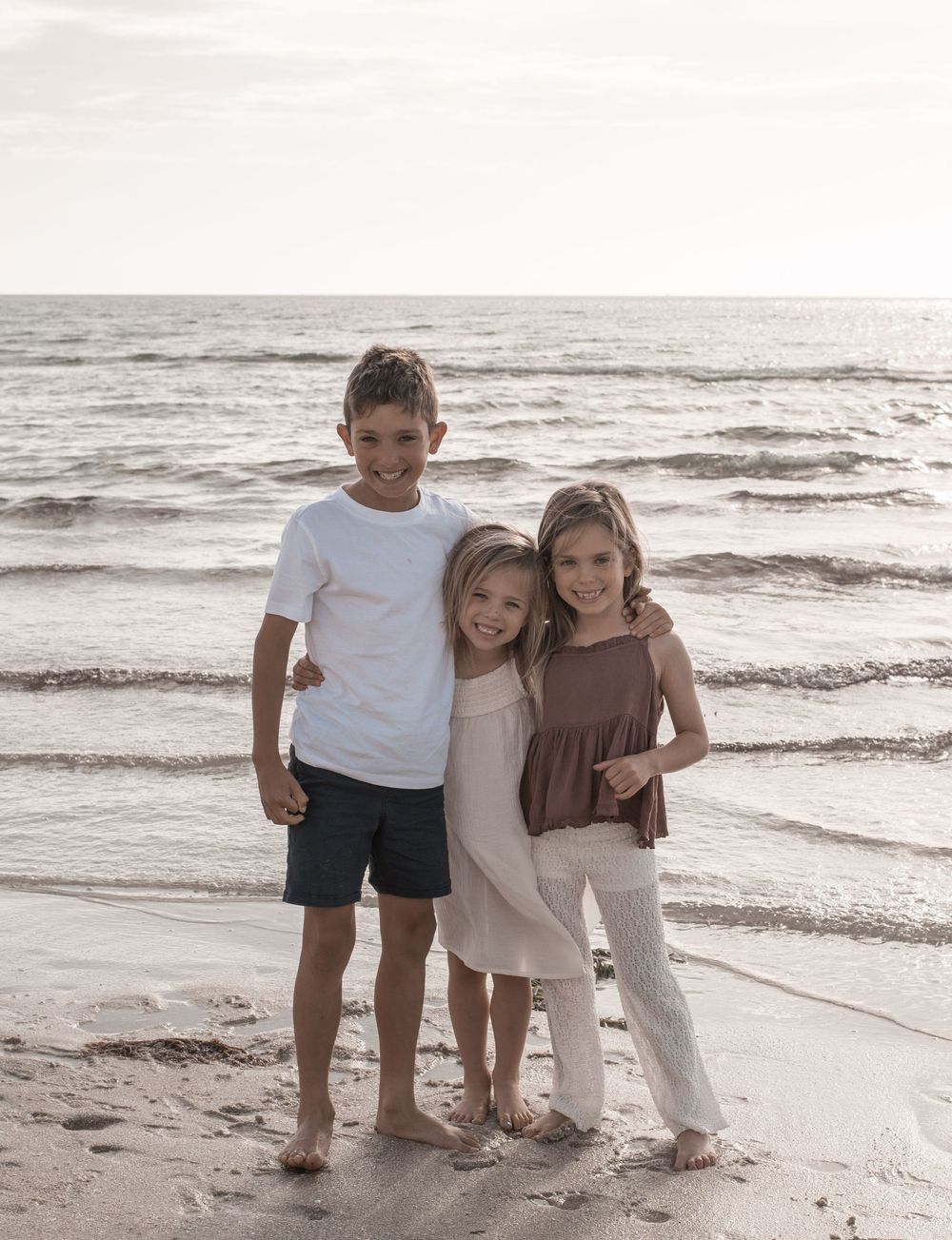 Children playing together on a sandy beach at sunset with gentle waves in the background.