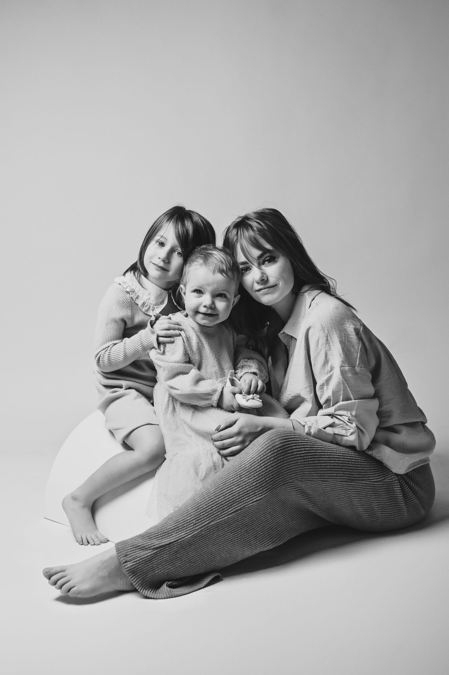 A black and white studio portrait showing a loving family moment with three people sitting together on the floor.