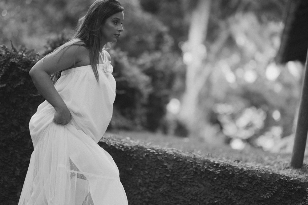 Black and white photo of a woman in a flowing white dress walking through a lush garden setting.