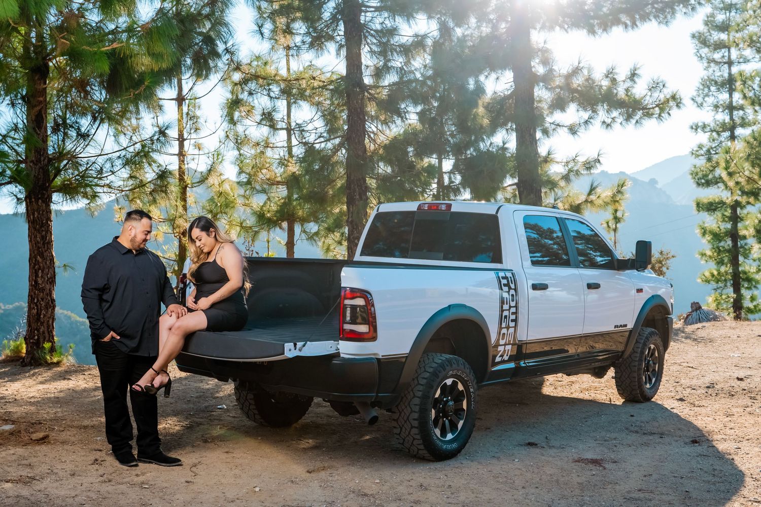 A white pickup truck parked on a scenic overlook with pine trees and mountains in the background.