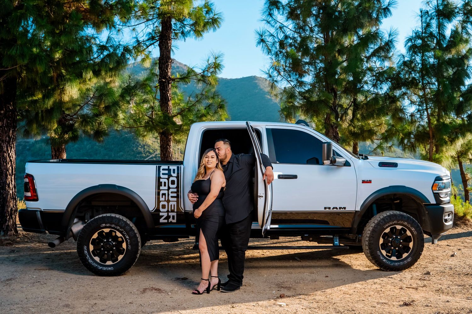 Couple embracing next to a white Ram pickup truck on a scenic mountain road.
