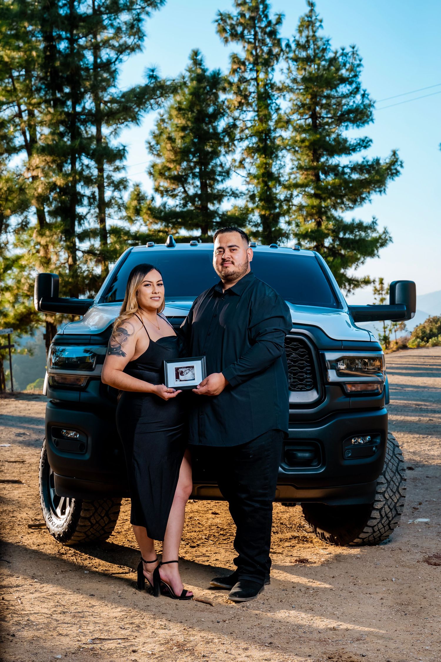 People holding a small box while posing in front of a customized black pickup truck.