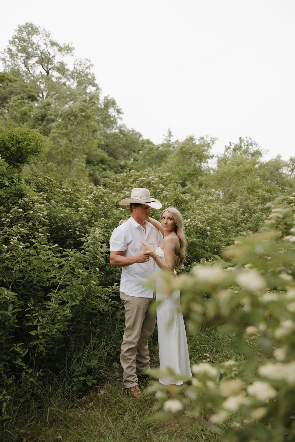 A romantic couple embraces in a lush green garden setting on a summer day.
