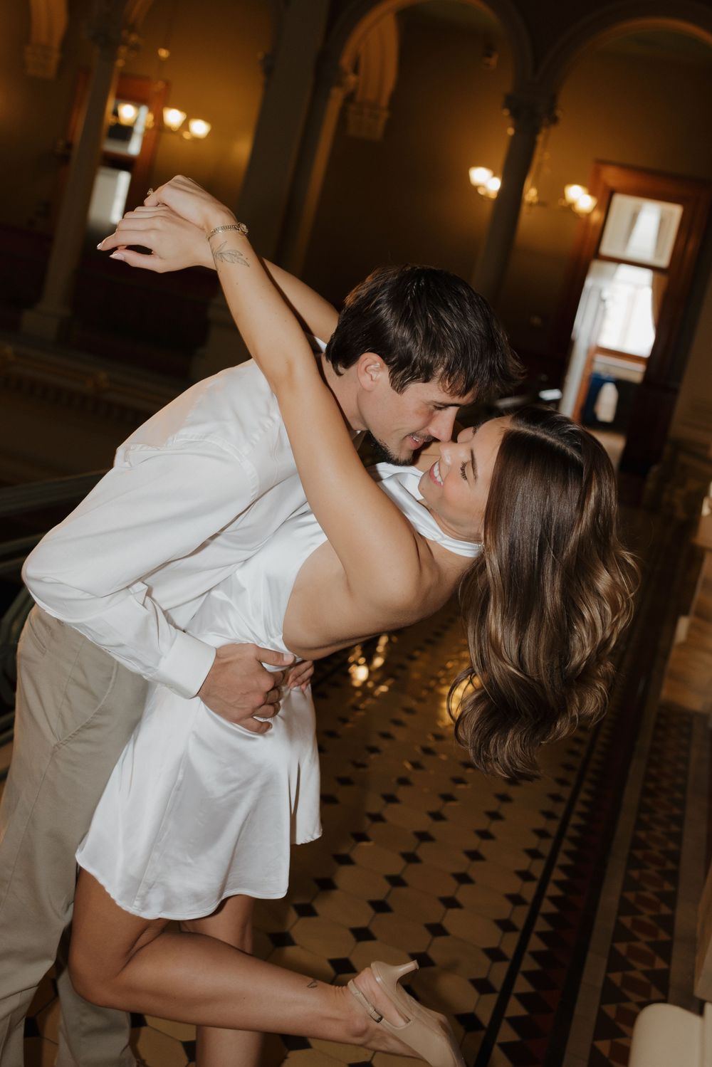 A couple shares a romantic dance together in an elegant ballroom with checkered floors and warm lighting.
