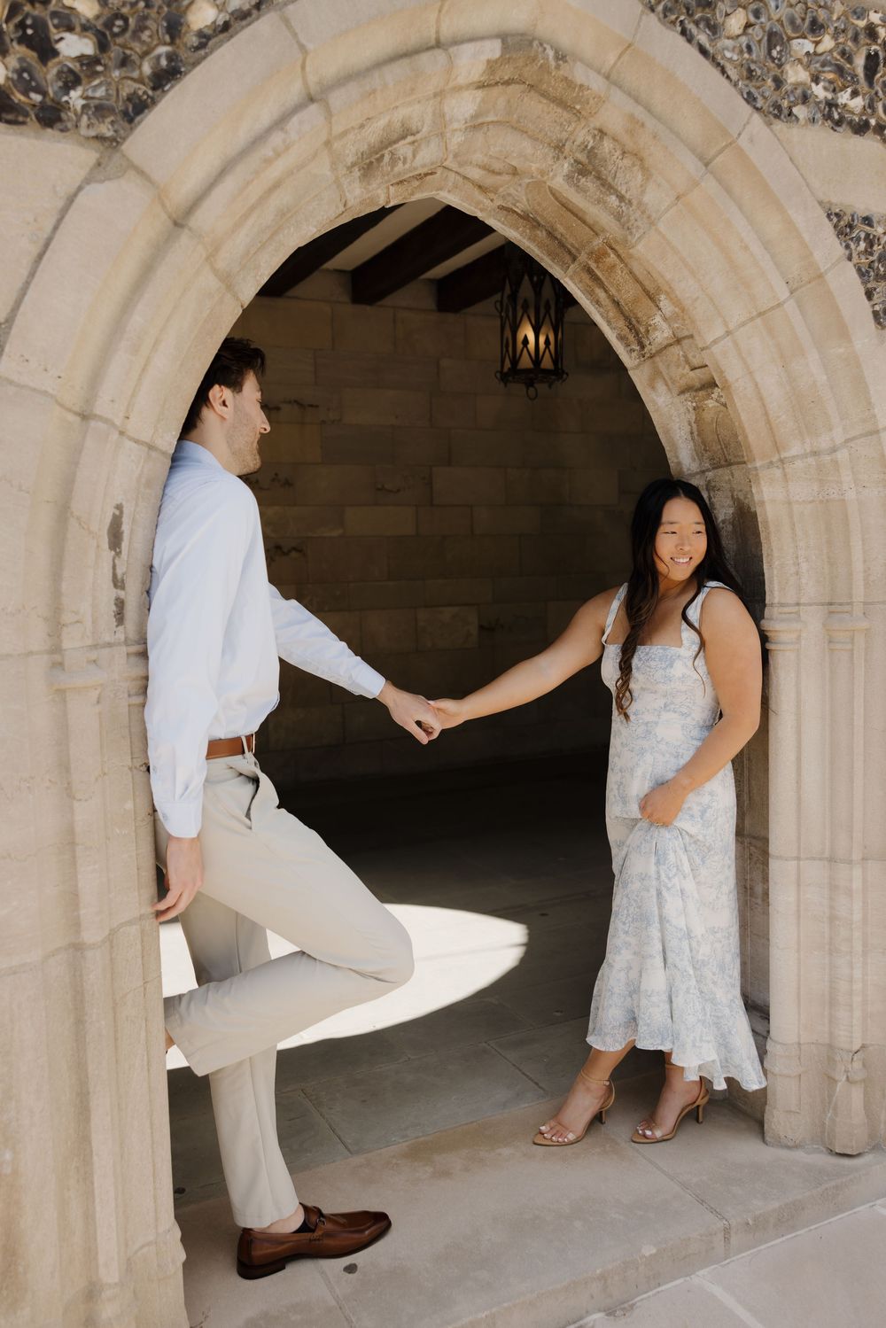 Couple sharing a romantic moment under a stone archway in elegant white attire.