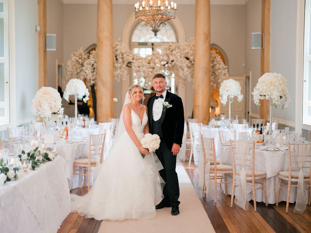 Elegant ballroom decorated with crystal chandeliers and white chairs for wedding reception.
