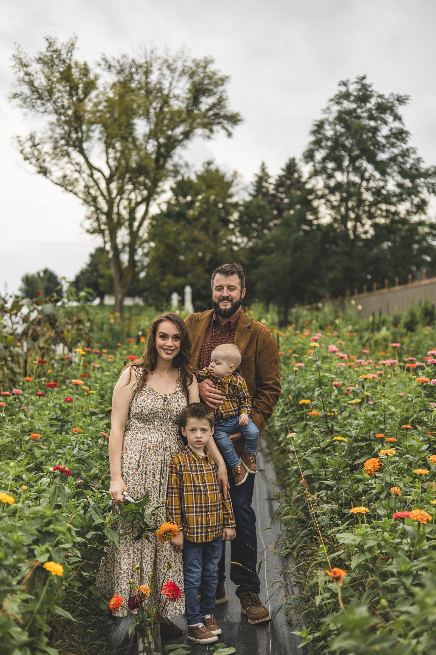 A family stands together on grass in front of red barns on a fall day.