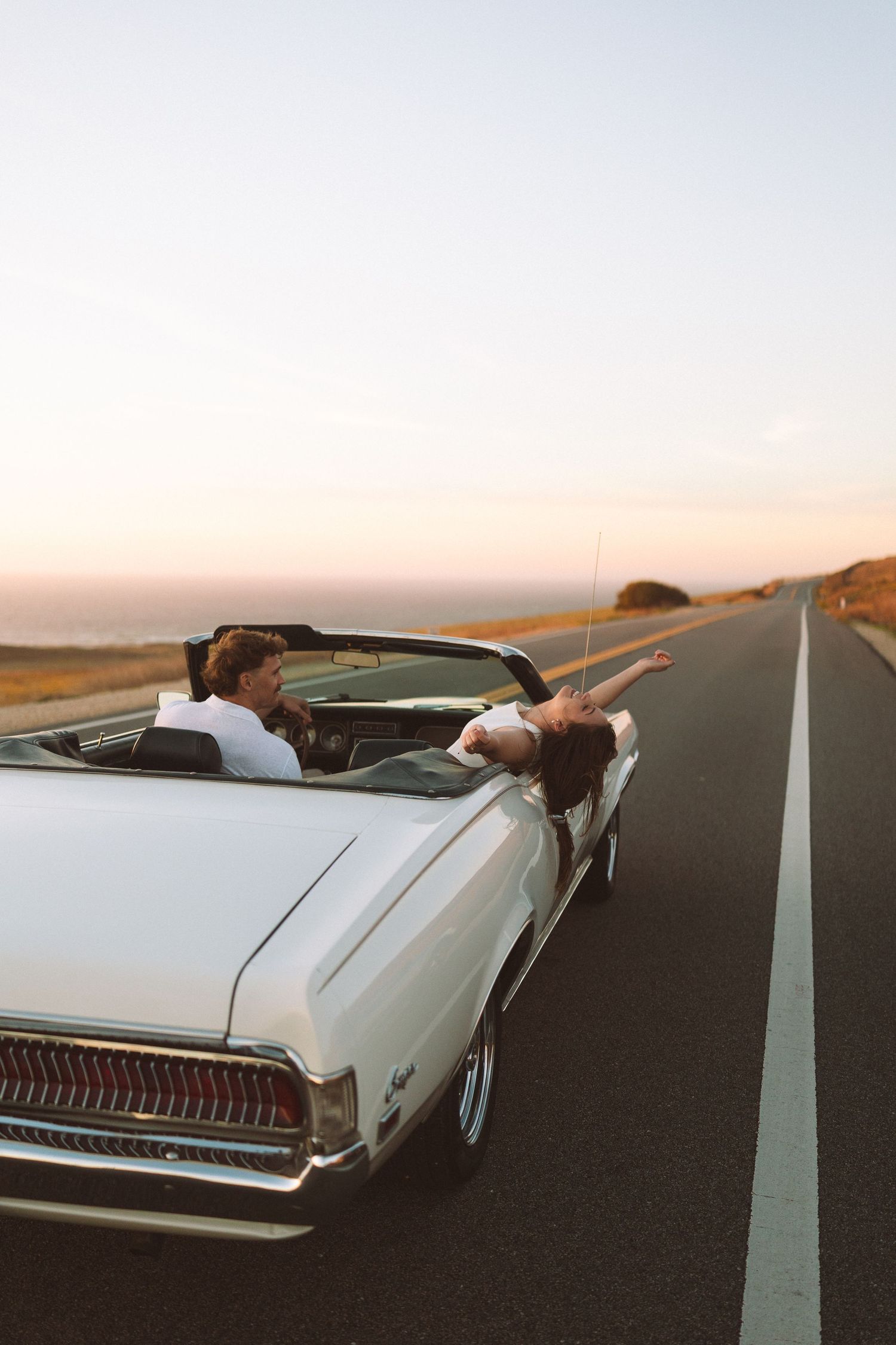Vintage white convertible car on empty road during sunset photoshoot.