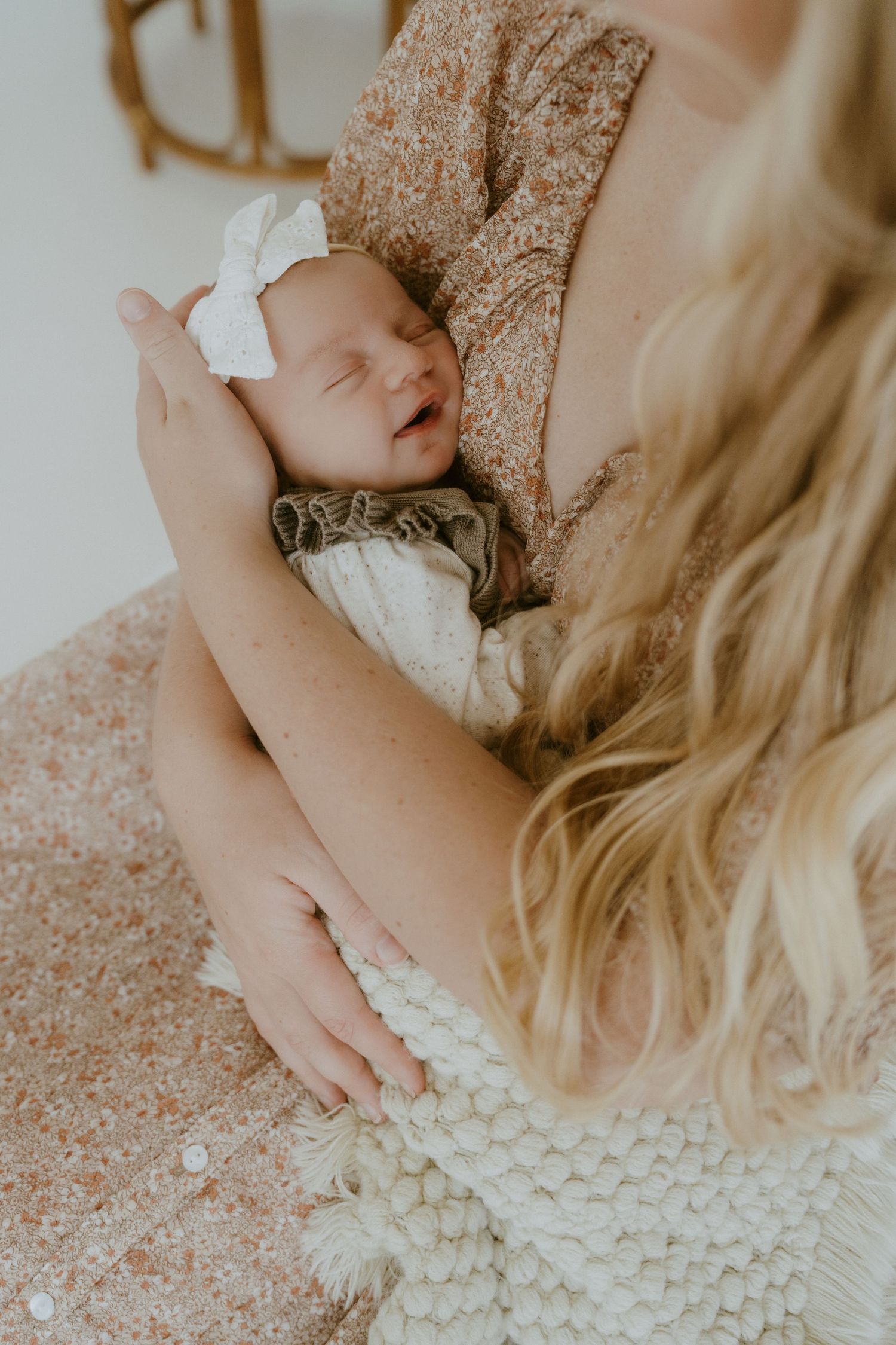 A sleeping newborn in white bow being held against floral fabric.