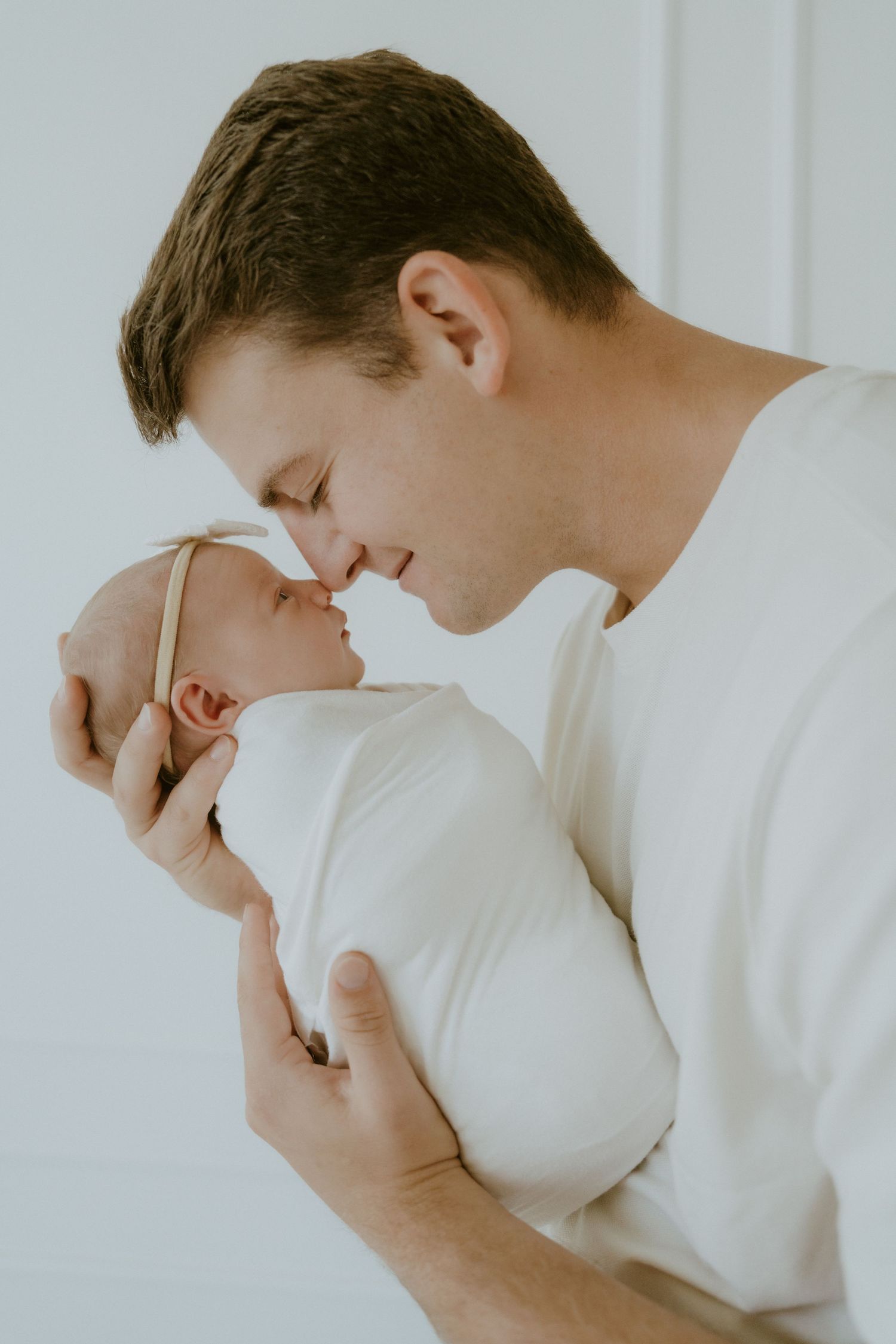 An intimate portrait of parent and newborn sharing a gentle moment against white background.