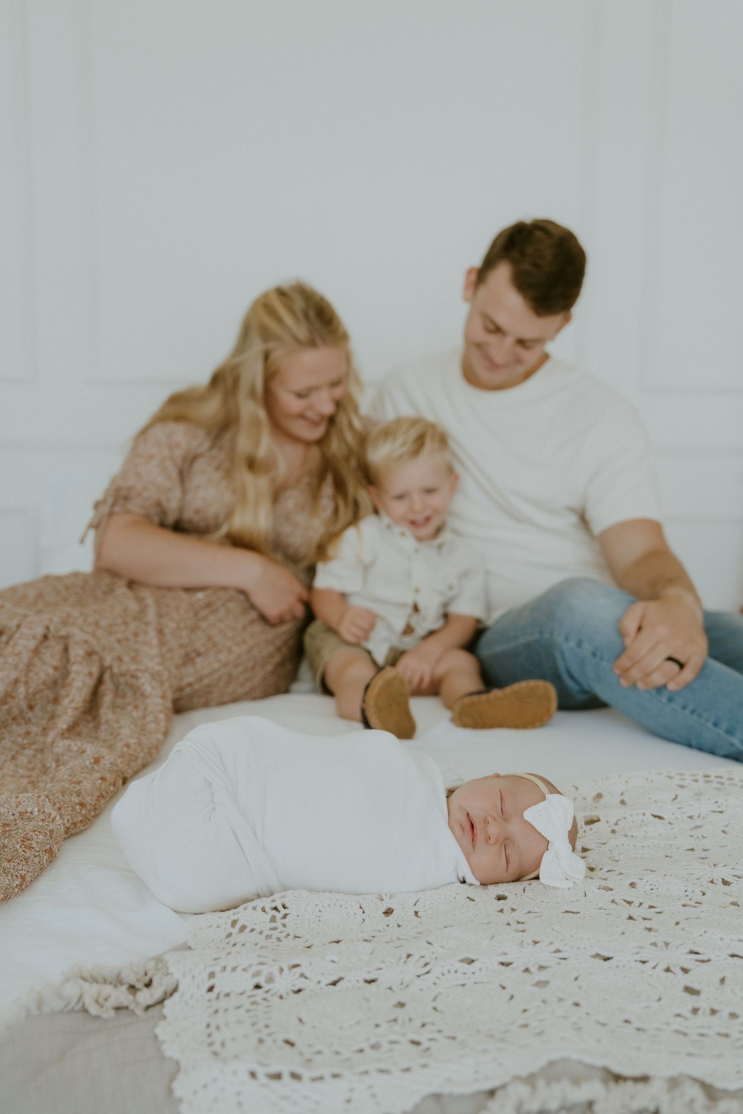 Family relaxing together on white floor with newborn and toddler.