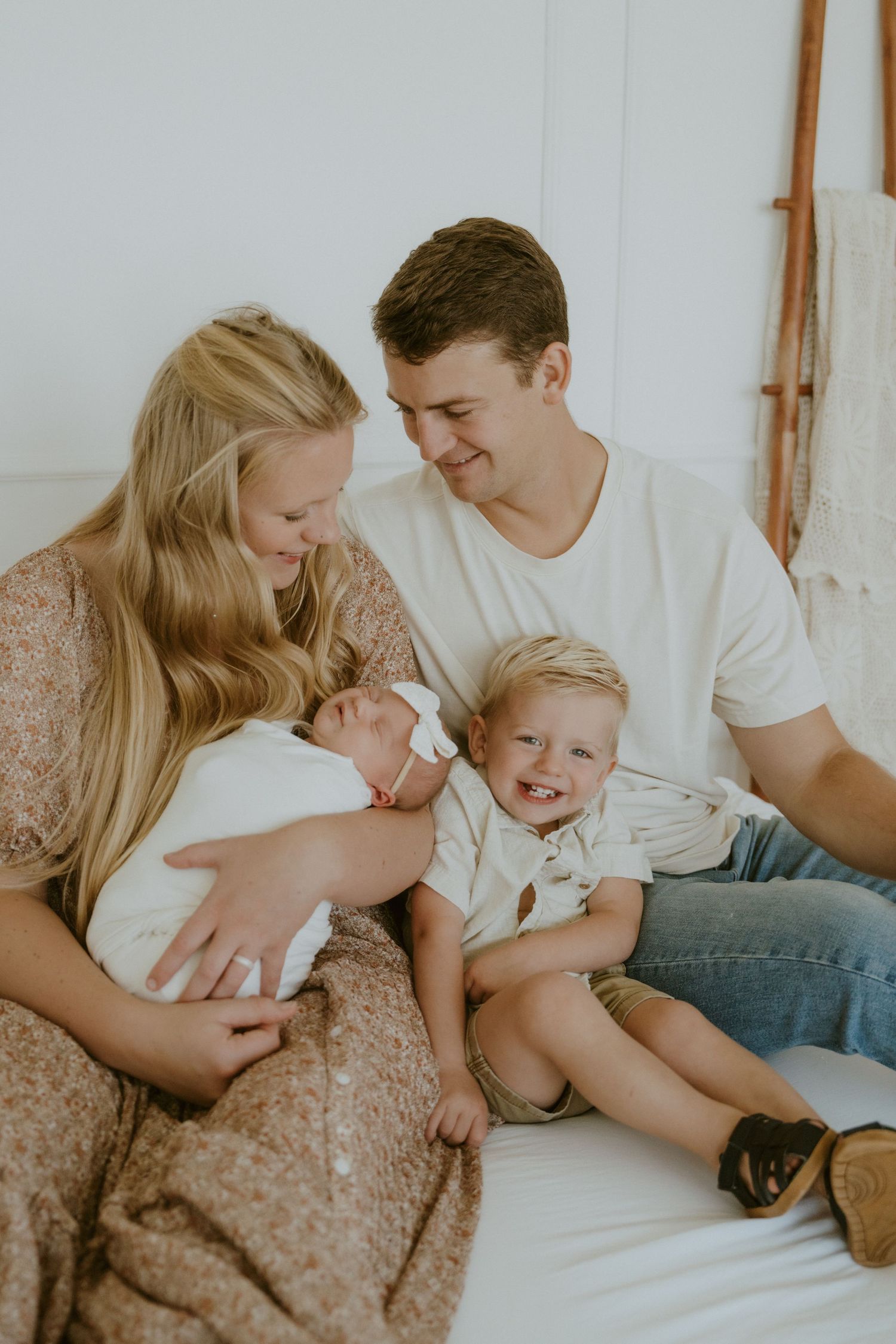 Family sharing intimate moment with newborn baby and toddler on white bed.