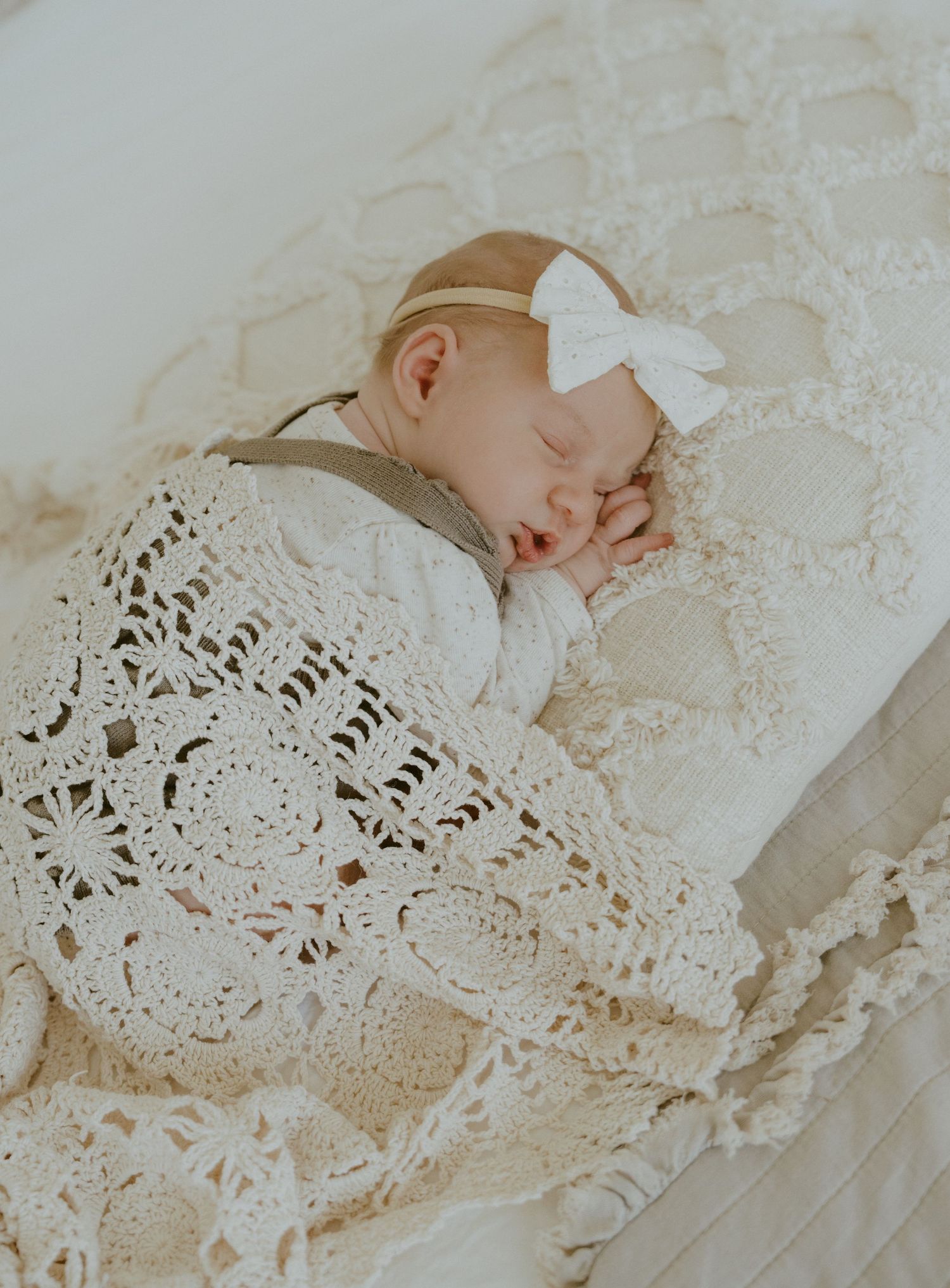 Sleeping newborn with white bow on lace blanket.