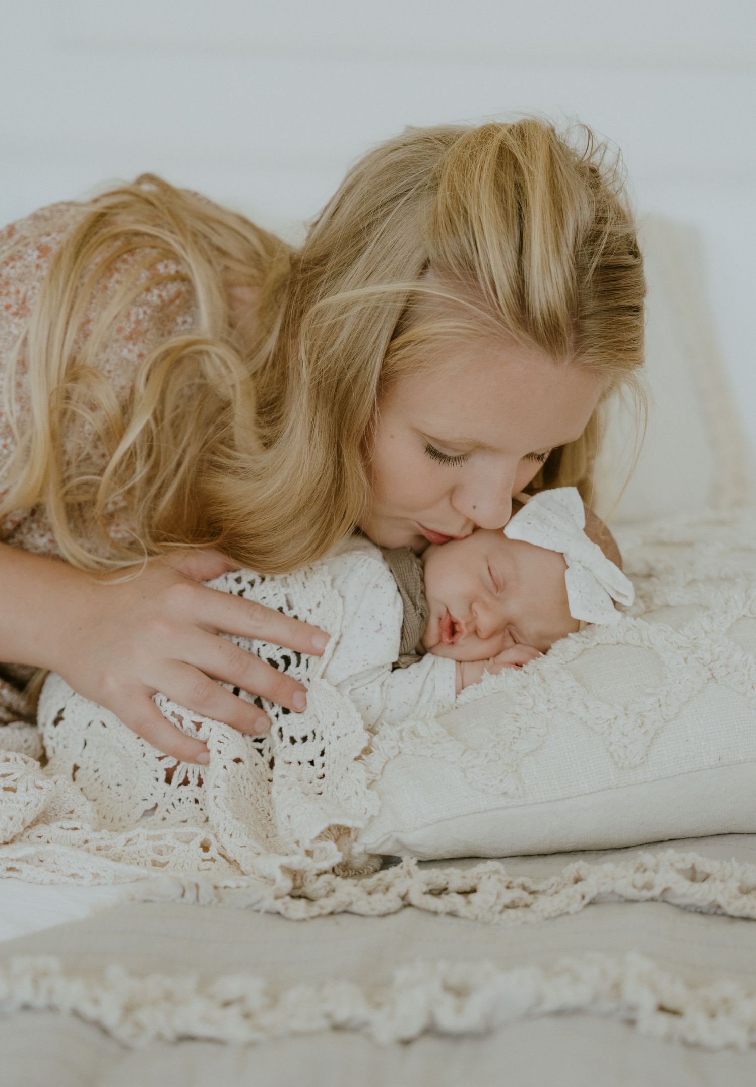 Mother giving gentle kiss to sleeping newborn on lace blanket.